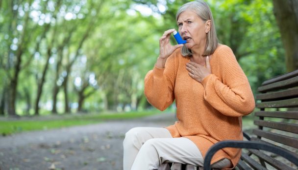 Older,Woman,Using,Inhaler,Seated,On,Park,Bench,Outdoors,,Managing