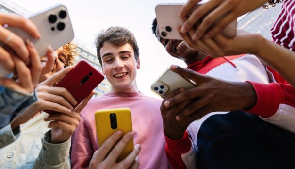 Young,Group,Of,Teen,Friends,Using,Mobile,Phone,Device,Standing